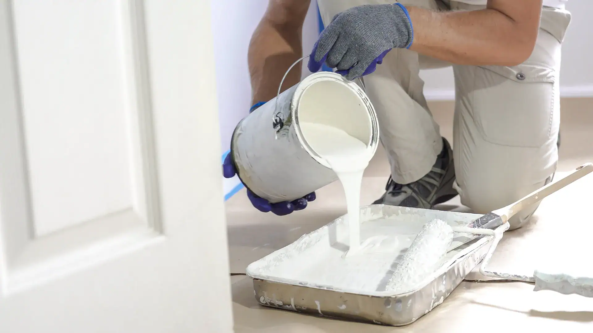 painter pouring white paint into a painter's tray to paint a bedroom in Peterborough County